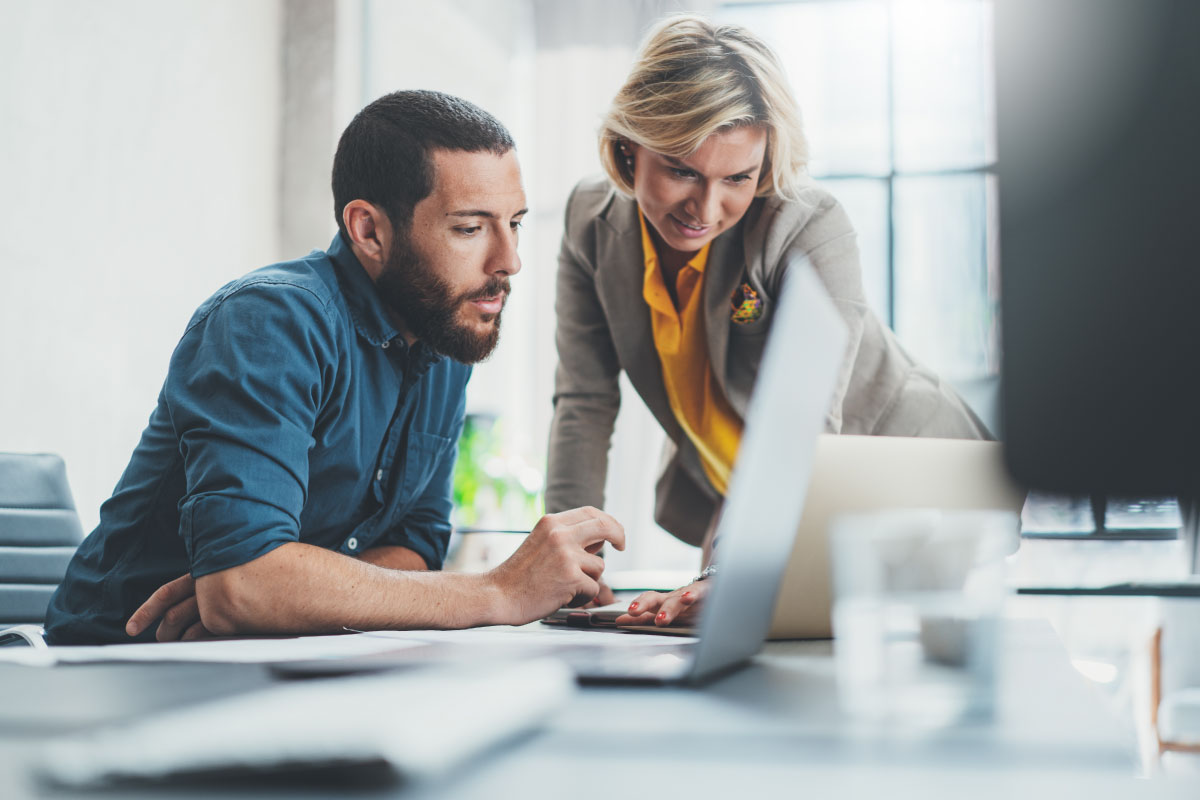 Two professionals reviewing Essential Eight readiness requirements and assessment information on a laptop.
