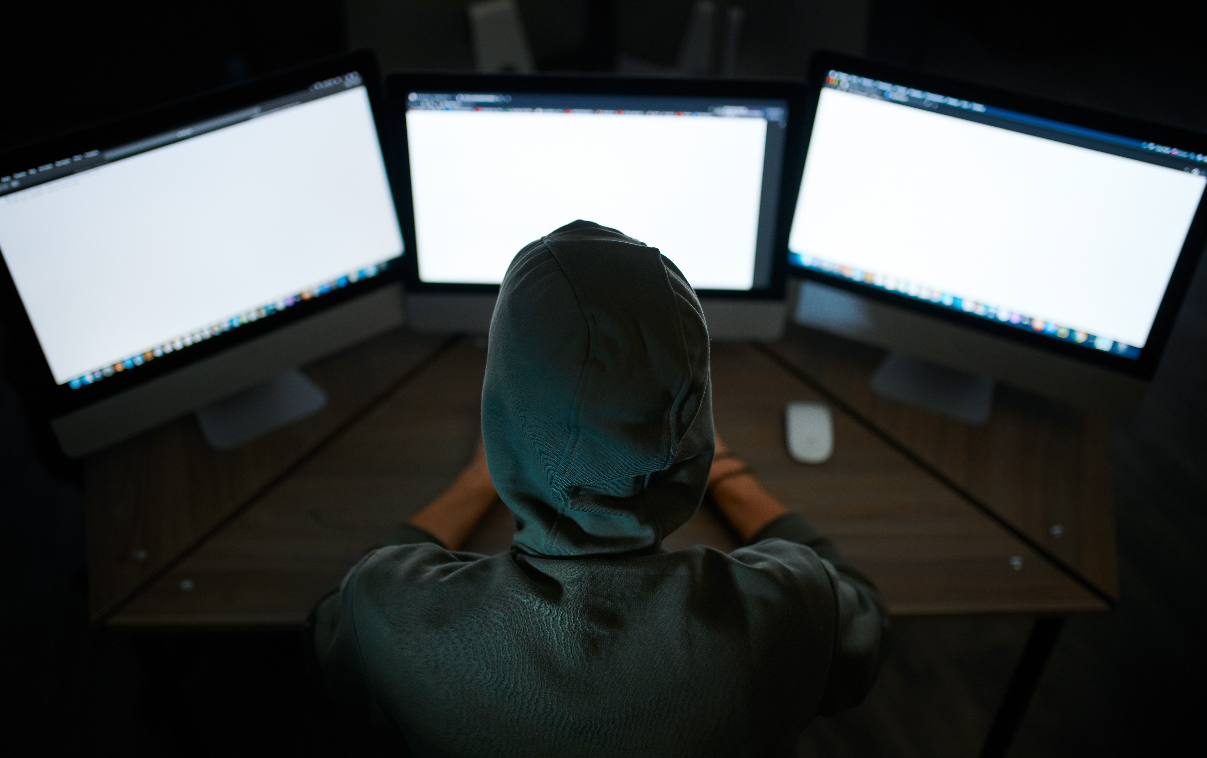 A hacker working behind 3 monitors infiltrating and organisations IT environment