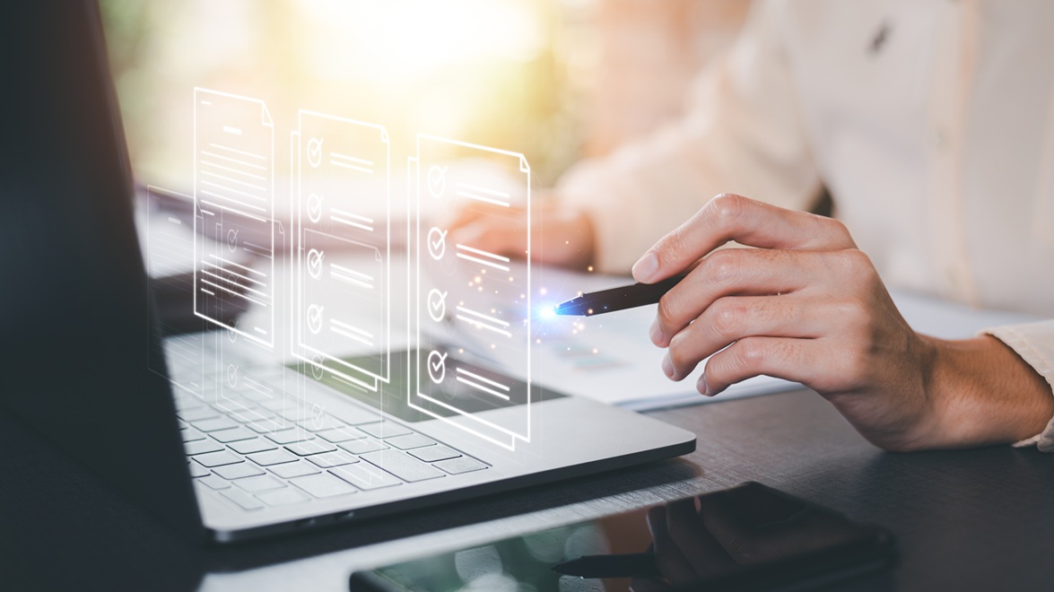A laptop on a desk with a businessman holding a pen pointing at an overlay of a graphic of a IT policy document, process document, and a procedure document