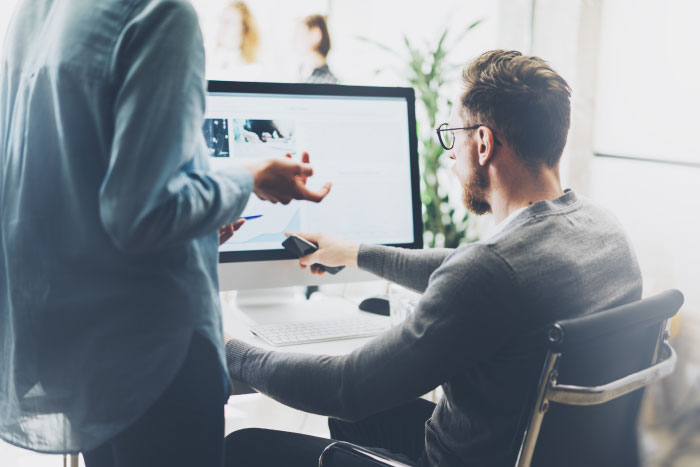 Two professionals reviewing Essential Eight controls and compliance requirements at a workstation.